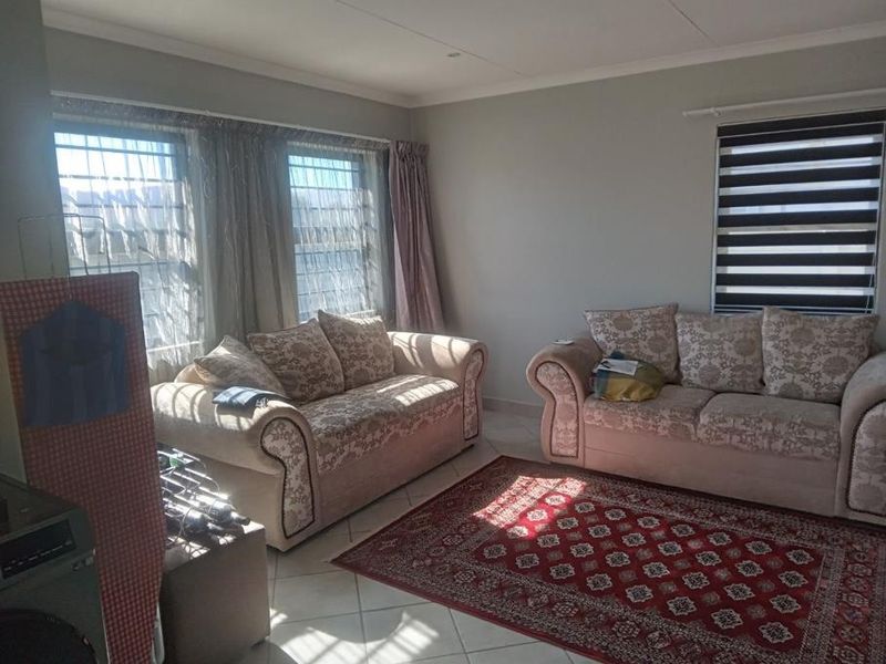 A living room featuring tiled flooring, security bars on the windows, and modern roller blinds, providing a functional and well-lit space.
