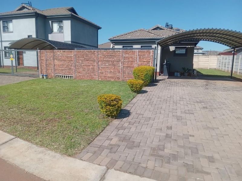 Front exterior view featuring a paved driveway, covered carport, brick boundary wall, and a well-maintained lawn area.