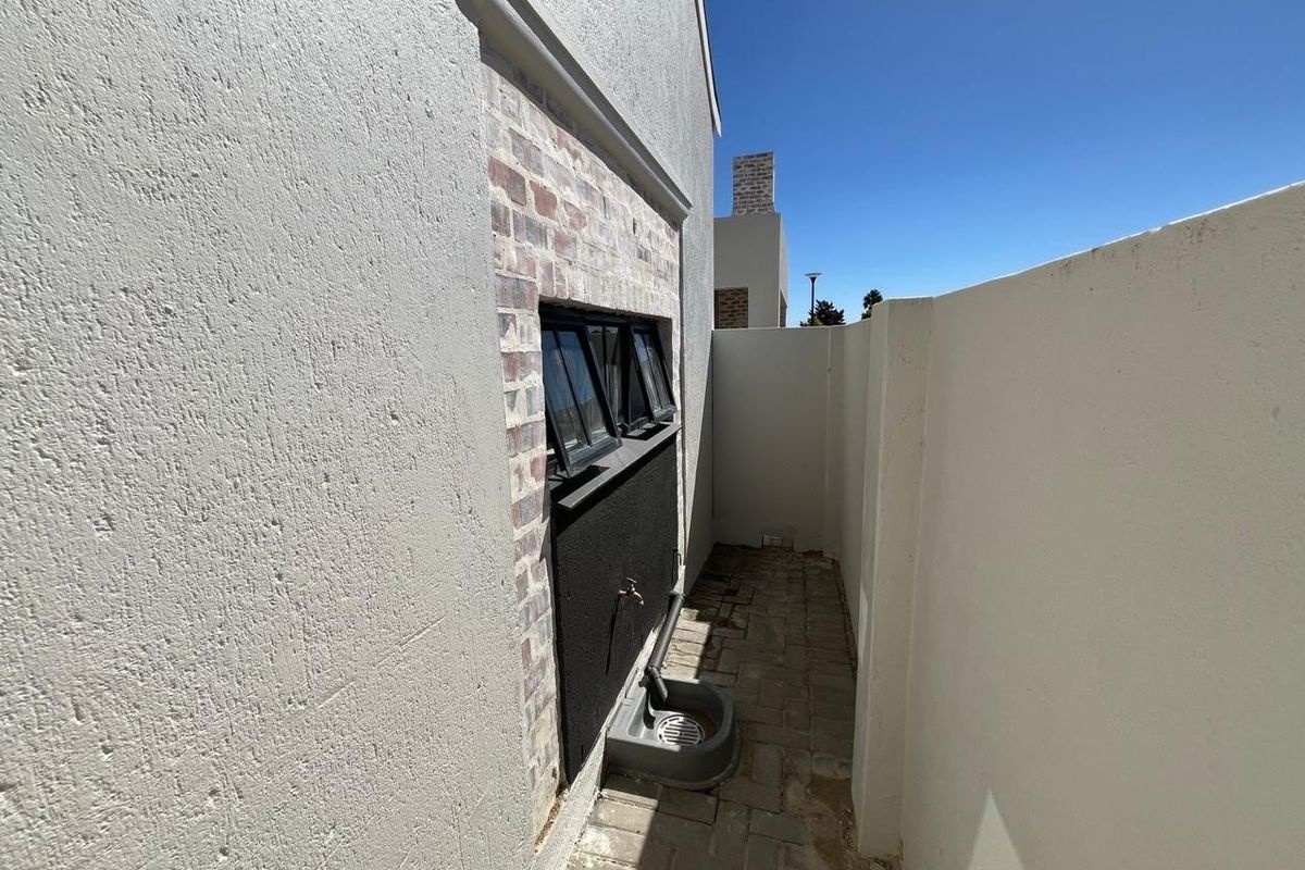 A narrow paved side passage featuring a brick-accented wall, external water tap with drainage, and secure boundary walling.