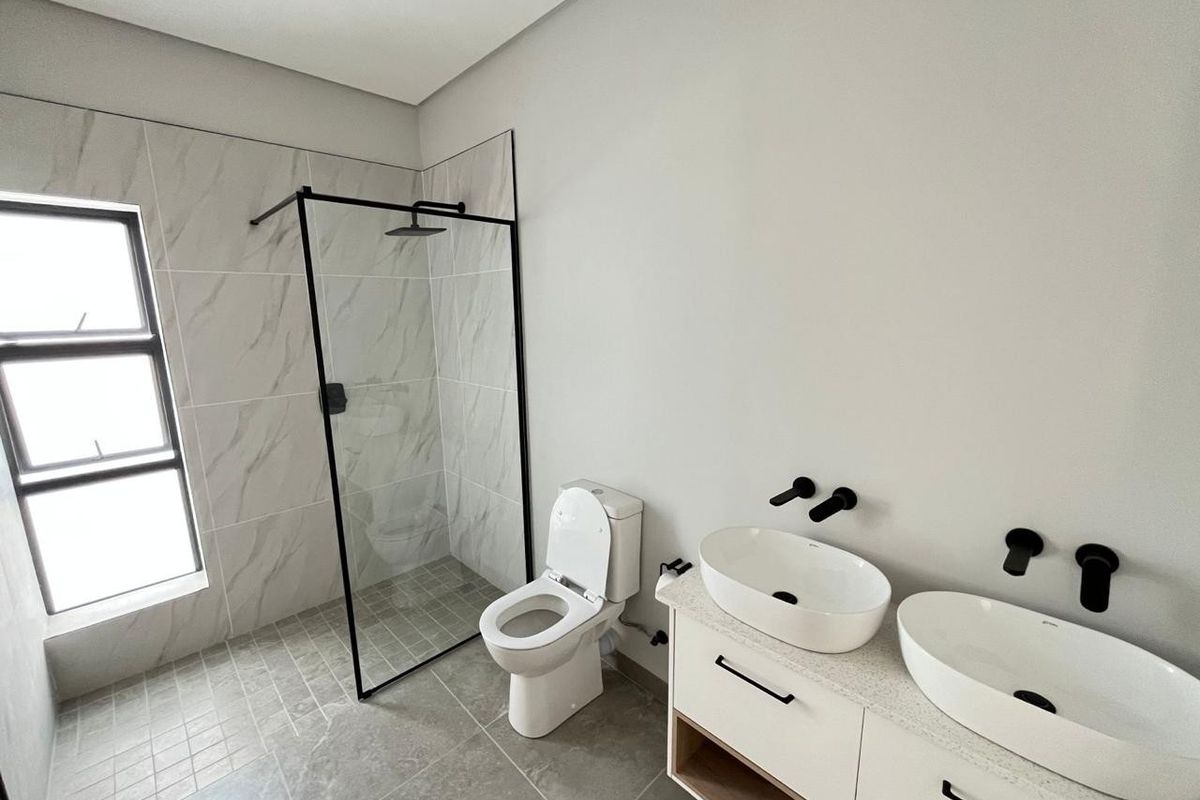 Modern bathroom featuring a walk-in shower with black frame, dual vessel sinks on a stone vanity, and contemporary wall-mounted fixtures.