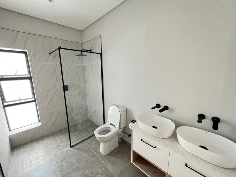 Modern bathroom featuring a walk-in shower with black frame, dual vessel sinks on a stone vanity, and contemporary wall-mounted fixtures.