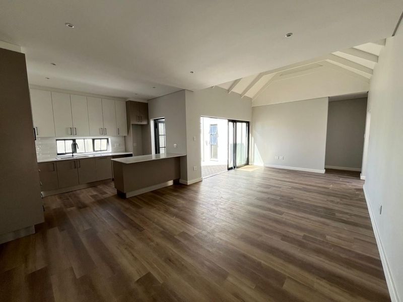 Spacious open-plan living and kitchen area featuring modern cabinetry, a kitchen island, vaulted ceilings, and sliding doors leading to an outdoor space.