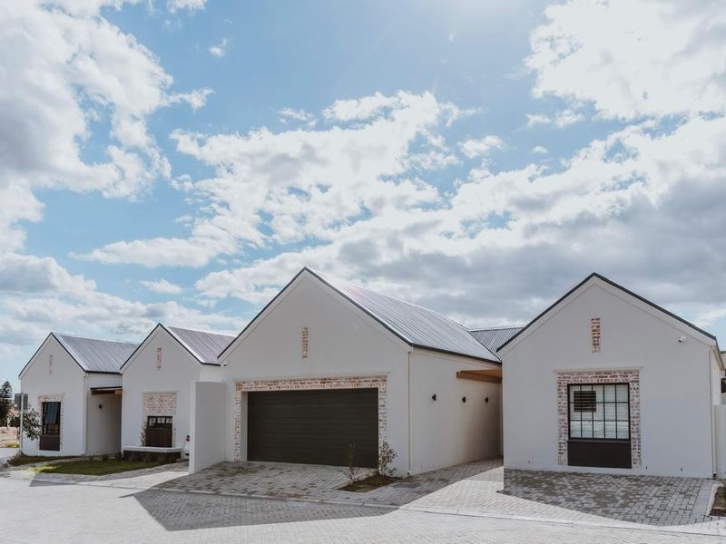 A modern retirement village residence featuring a clean white facade, metal roofing, and a paved driveway with integrated garage access.