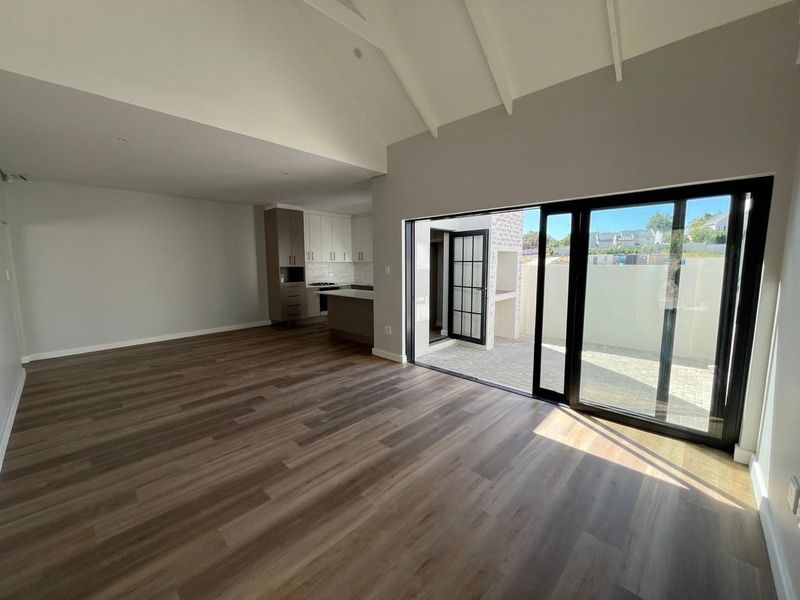 Spacious open-plan living area featuring vaulted ceilings, modern laminate flooring, and large sliding doors opening to a private patio with a built-in braai.