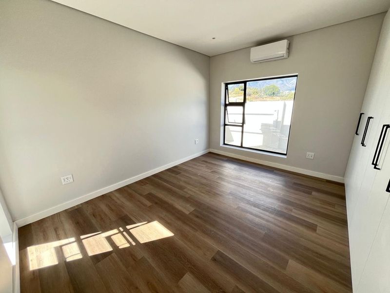 A bright, modern bedroom featuring neutral walls, durable laminate flooring, built-in wardrobes, and a wall-mounted air conditioning unit.