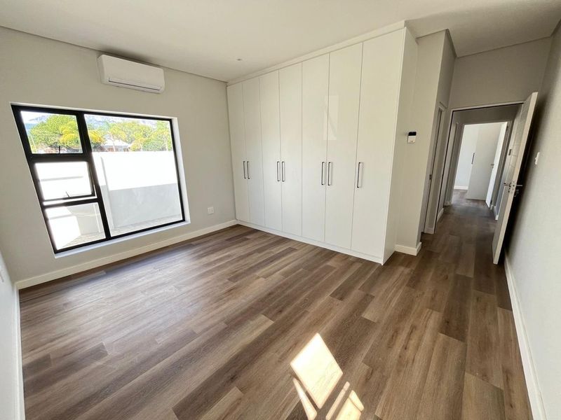 A bright, modern bedroom featuring sleek built-in cupboards, durable laminate flooring, and a wall-mounted air conditioning unit.