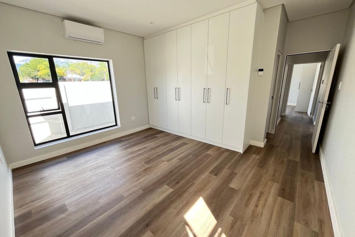 A bright, modern bedroom featuring sleek built-in cupboards, durable laminate flooring, and a wall-mounted air conditioning unit.