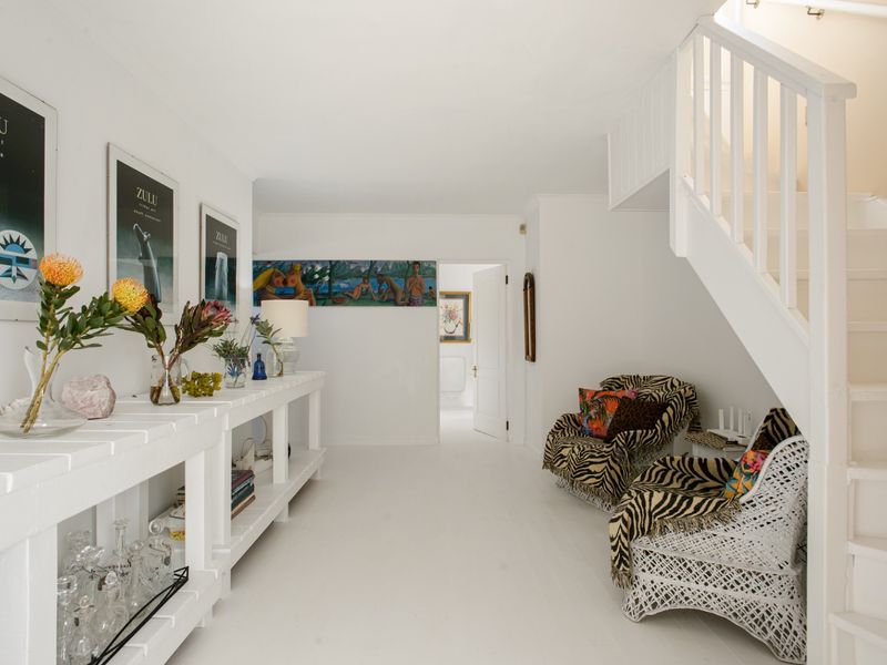 A bright and airy entrance hall featuring a white staircase with a wooden balustrade and built-in shelving units.