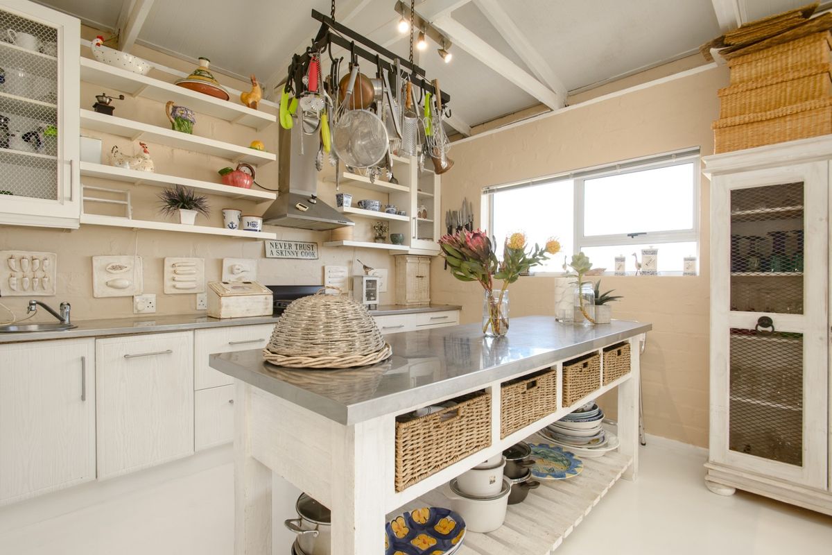 A charming kitchen featuring open shelving, stainless steel countertops, exposed ceiling beams, and a central island with integrated storage.