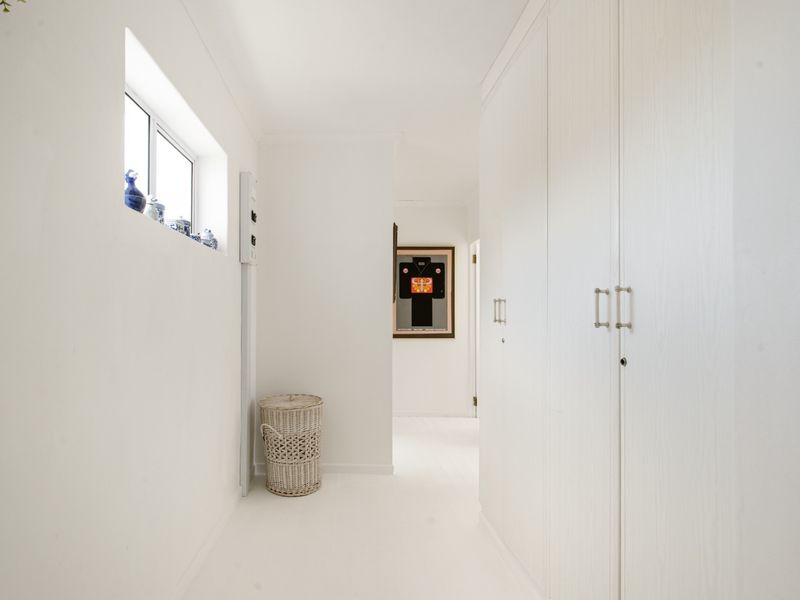 A bright, minimalist hallway featuring extensive built-in storage cupboards and clean white finishes throughout.