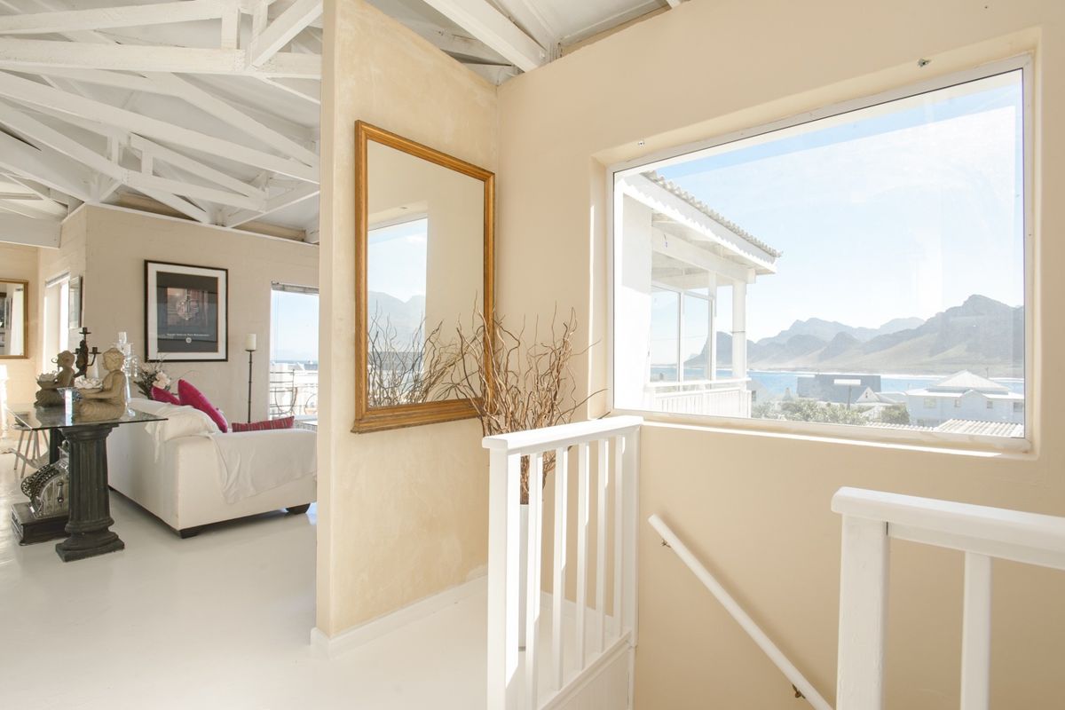 Bright living area featuring exposed white roof trusses, a staircase with a white railing, and a large window offering scenic coastal and mountain views.