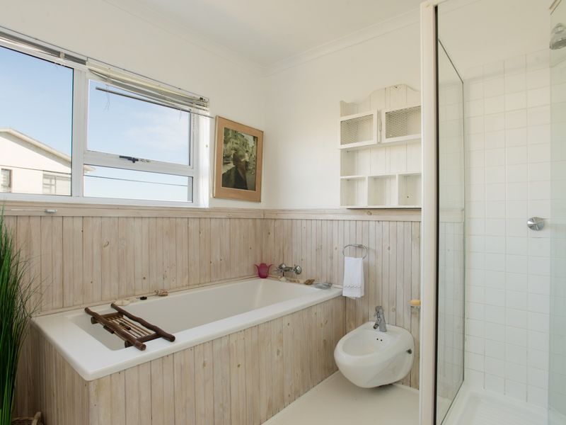 A bathroom featuring a built-in bathtub with timber paneling, a separate shower enclosure, and a bidet, finished with light-toned wall cladding.