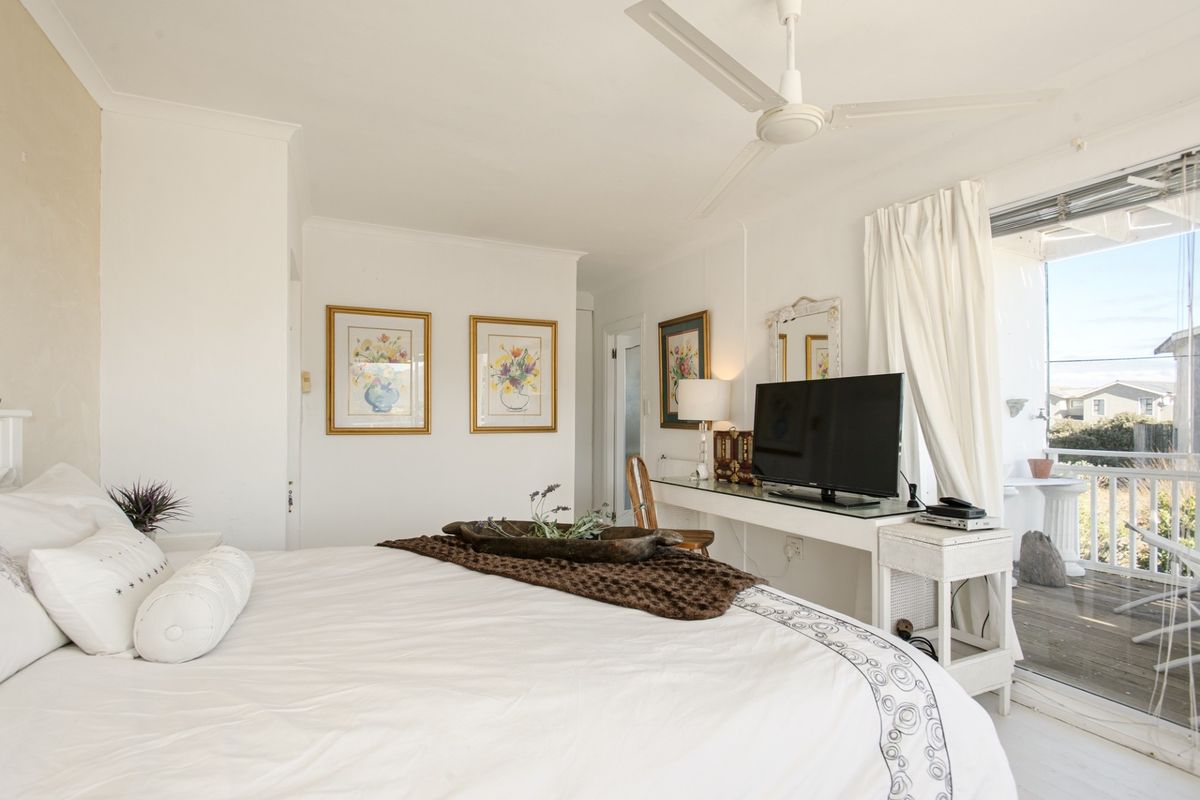 A bright bedroom featuring a ceiling fan and direct access to an outdoor balcony through sliding glass doors.