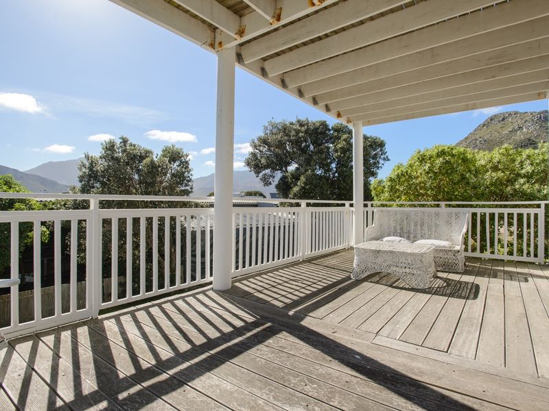 A spacious elevated balcony featuring timber decking, a white balustrade, and a covered pergola, offering scenic mountain views.