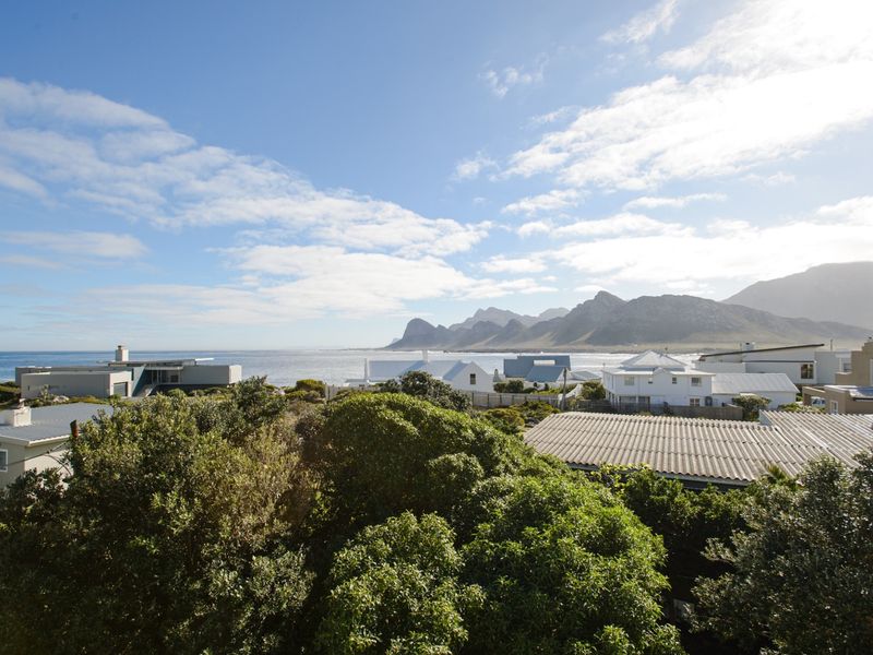 A scenic elevated view overlooking the coastal neighbourhood, surrounding residential properties, and distant mountain ranges.