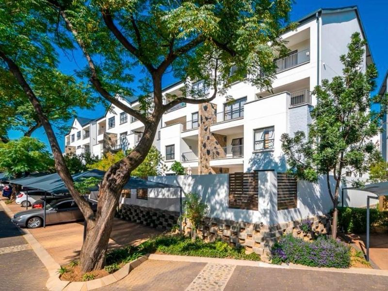 Exterior view of a modern apartment complex featuring stone cladding, private balconies, and covered parking bays within a landscaped setting.
