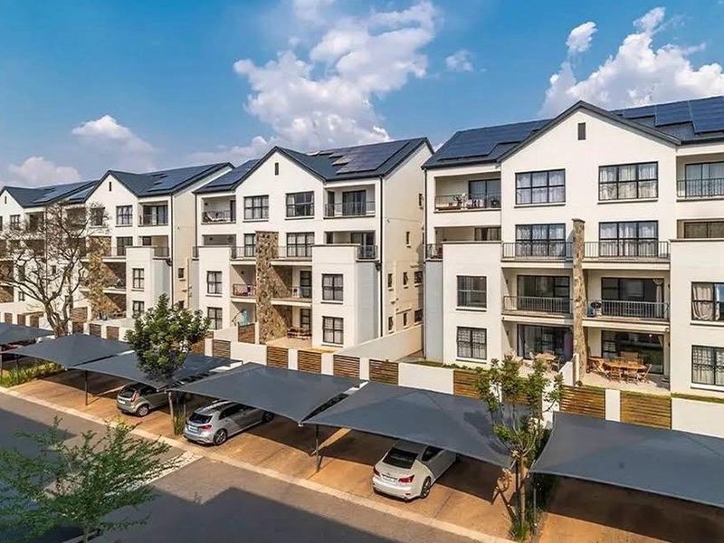 A modern multi-story apartment complex featuring solar panels, private balconies, and dedicated covered parking bays for residents.