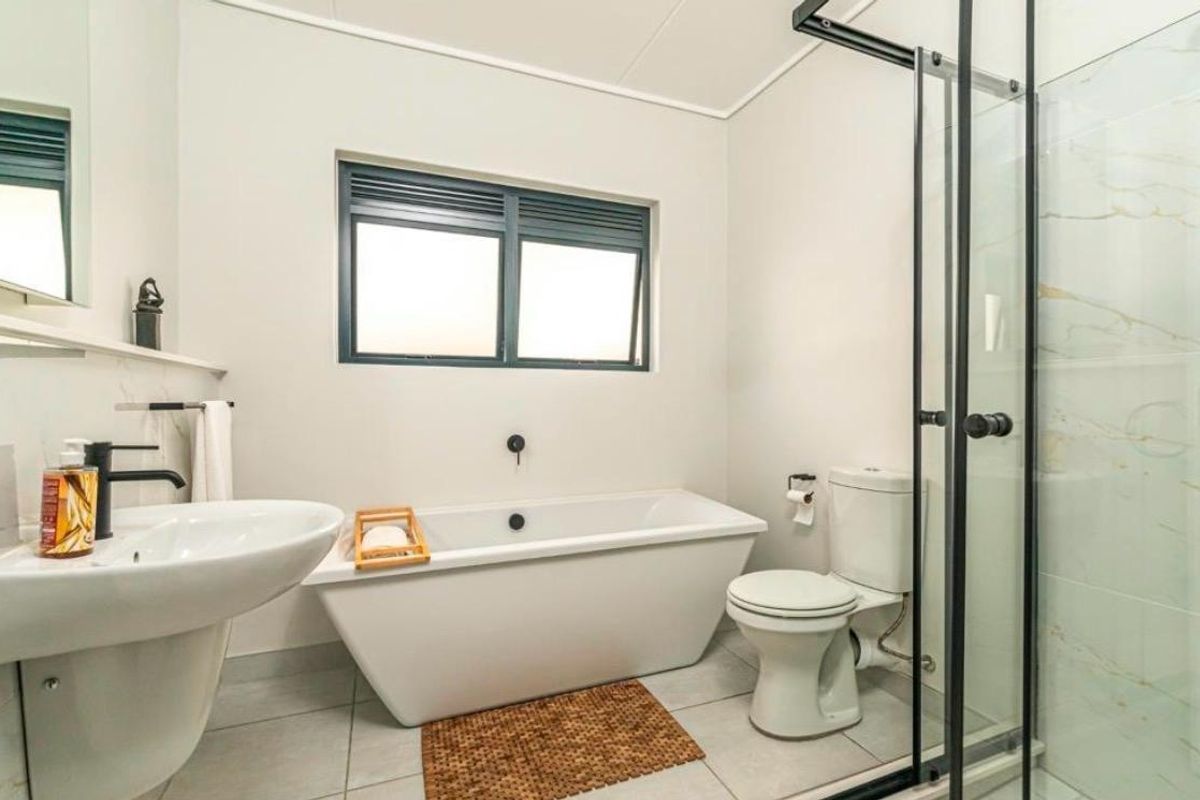 Modern bathroom featuring a freestanding bathtub, separate glass-enclosed shower, pedestal basin, and toilet with neutral tiled finishes.