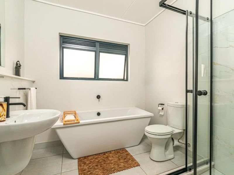 Modern bathroom featuring a freestanding bathtub, separate glass-enclosed shower, pedestal basin, and toilet with neutral tiled finishes.