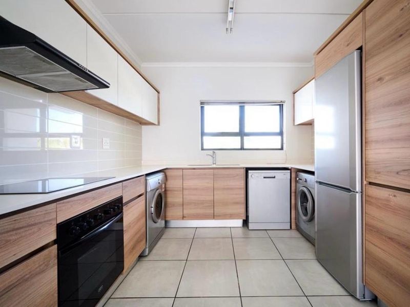 Modern kitchen featuring wood-grain cabinetry, white countertops, tiled flooring, and integrated appliance spaces, offering a clean and functional layout.