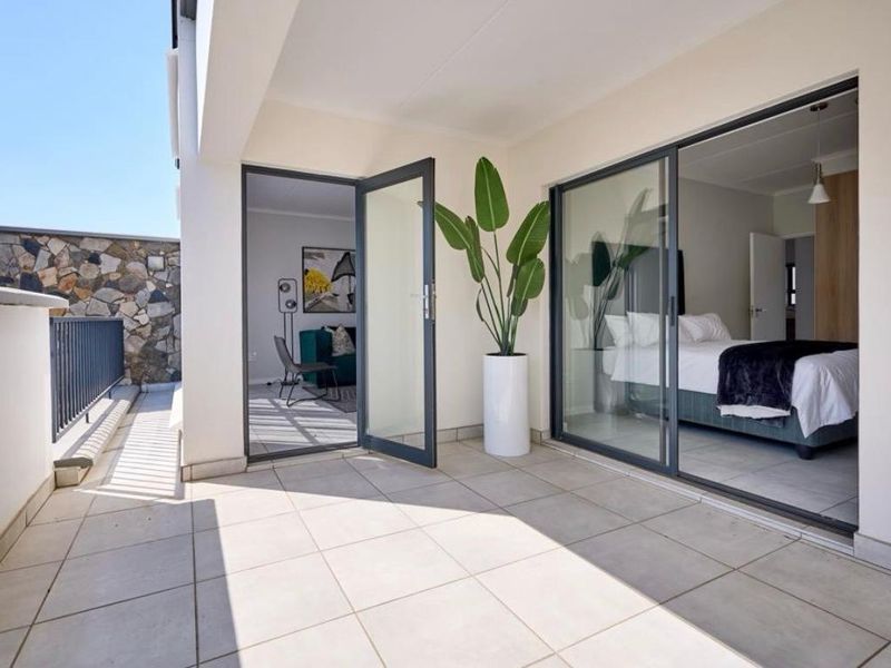 A modern, well-maintained balcony featuring tiled flooring, a metal balustrade, and a stone feature wall, providing seamless access to the interior living spaces.