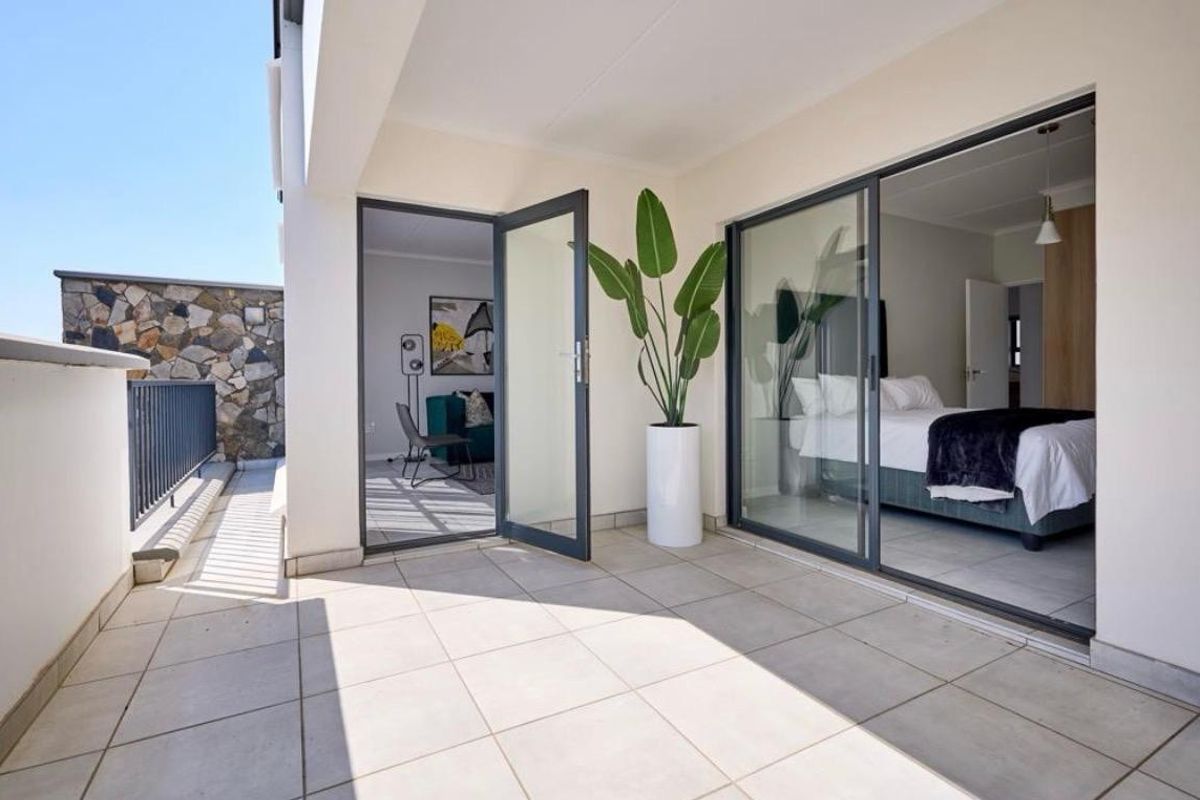 A modern, well-maintained balcony featuring tiled flooring, a metal balustrade, and a stone feature wall, providing seamless access to the interior living spaces.