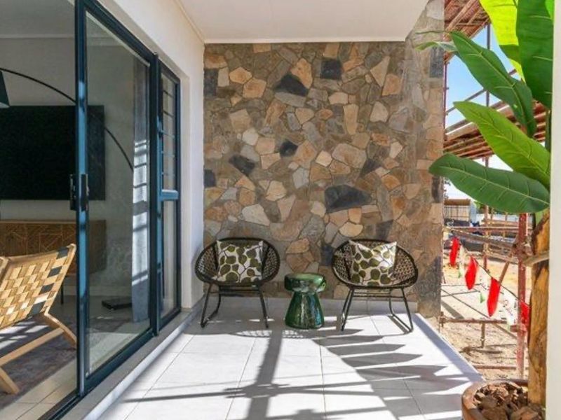A covered patio featuring tiled flooring and a decorative stone cladding feature wall, providing seamless access to the interior living space through sliding glass doors.