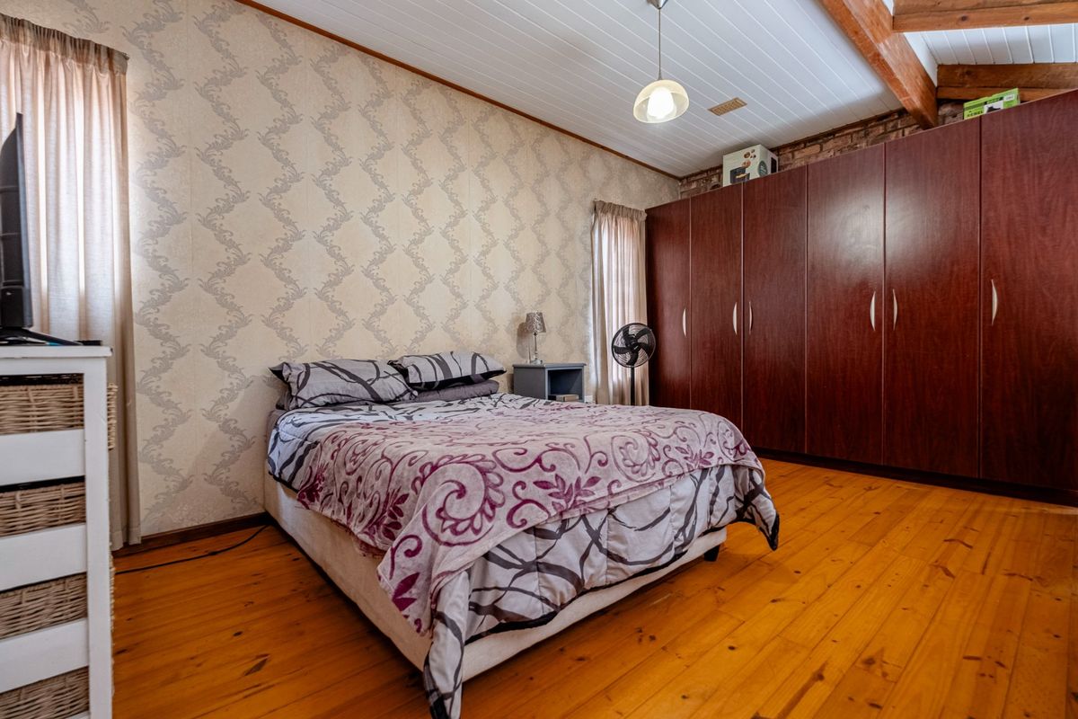 A bedroom featuring timber flooring, exposed ceiling beams, and a large built-in wardrobe with dark wood finish.