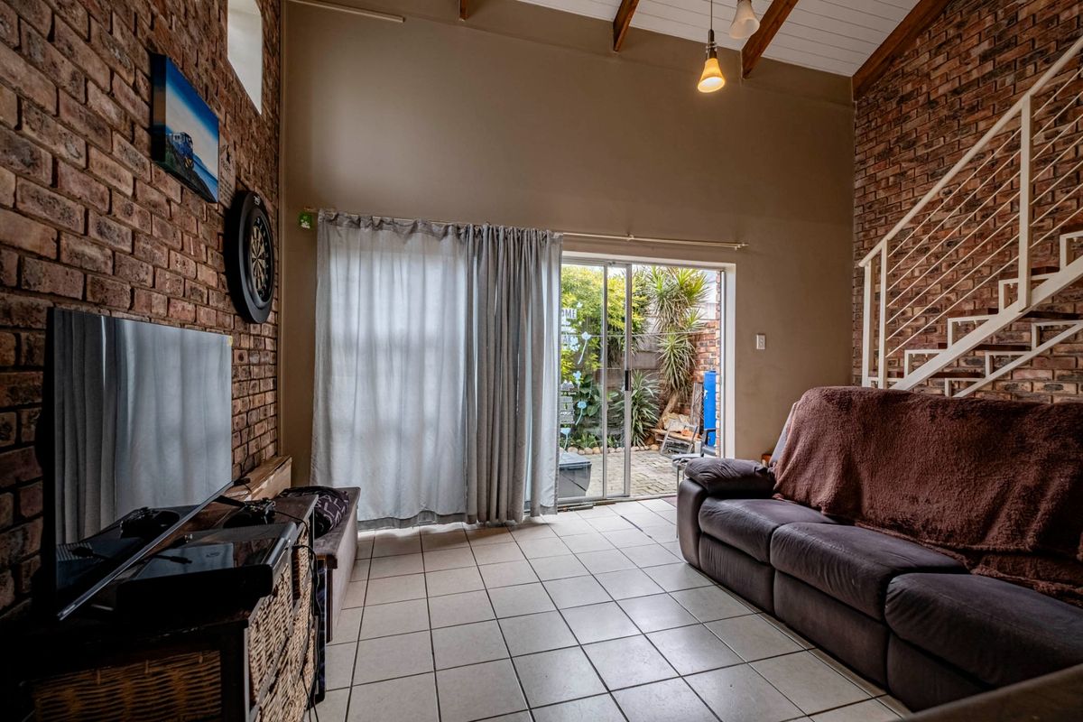 Living room featuring exposed brick walls, vaulted ceilings with exposed beams, tiled flooring, and a sliding glass door providing access to the outdoor area.
