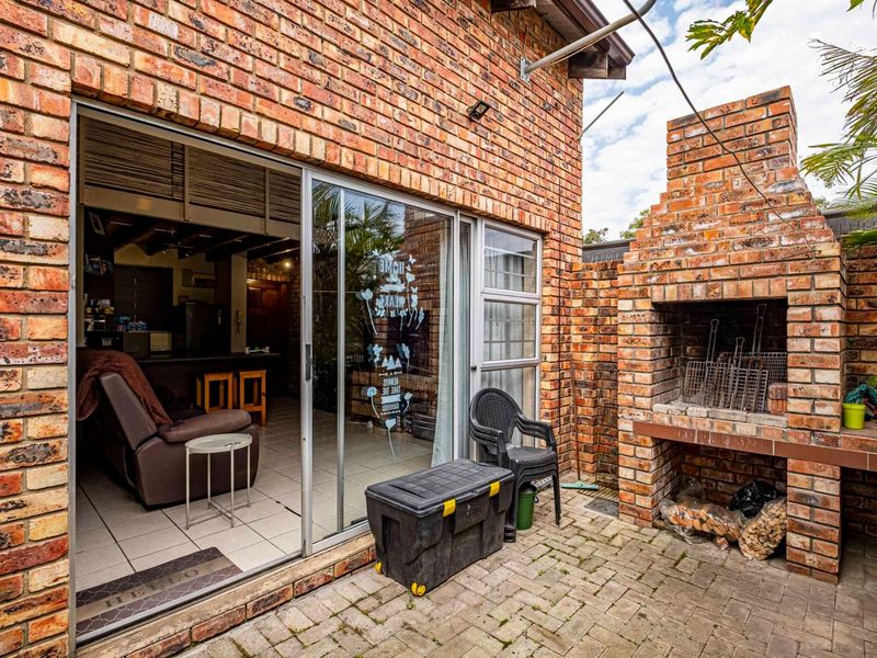 Outdoor patio area featuring exposed brick walls, paved flooring, and a built-in brick braai, providing direct access to the interior living space.