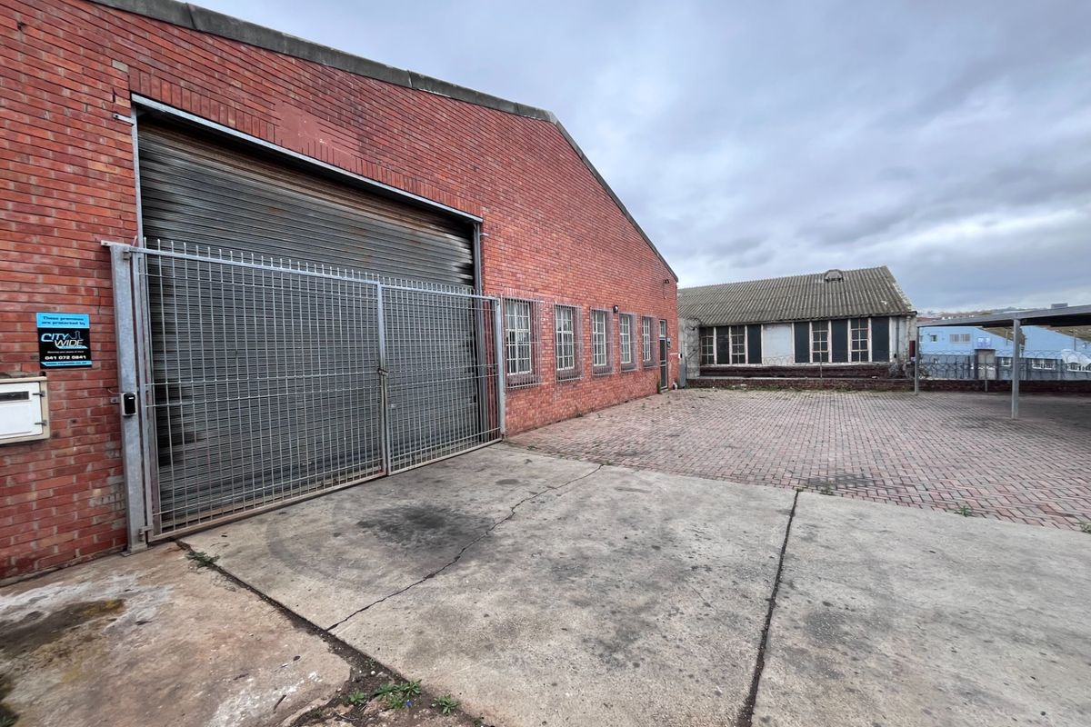 Industrial rear yard featuring a brick warehouse building with a large roller shutter door, security fencing, and paved outdoor space.