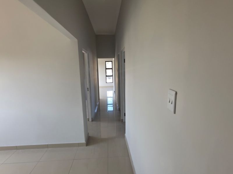 A clean, neutral hallway featuring tiled flooring and smooth walls, providing access to multiple rooms within the property.