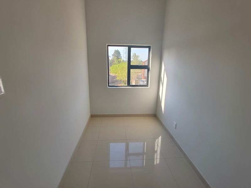 A clean, empty bedroom featuring neutral tiled flooring, smooth walls, and a single window providing natural light.
