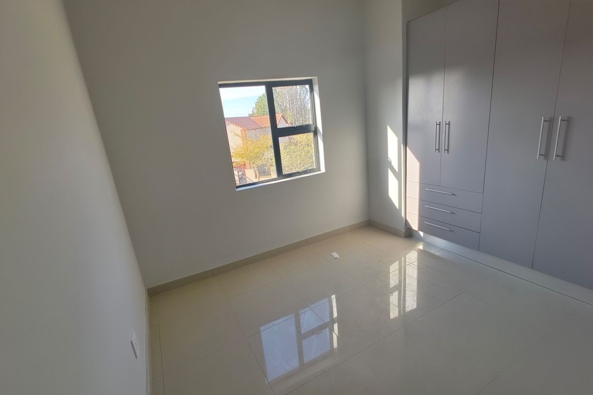 A bright, empty bedroom featuring neutral tiled flooring and modern built-in cupboards with clean lines and ample storage space.