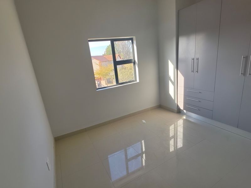 A bright, empty bedroom featuring neutral tiled flooring and modern built-in cupboards with clean lines and ample storage space.