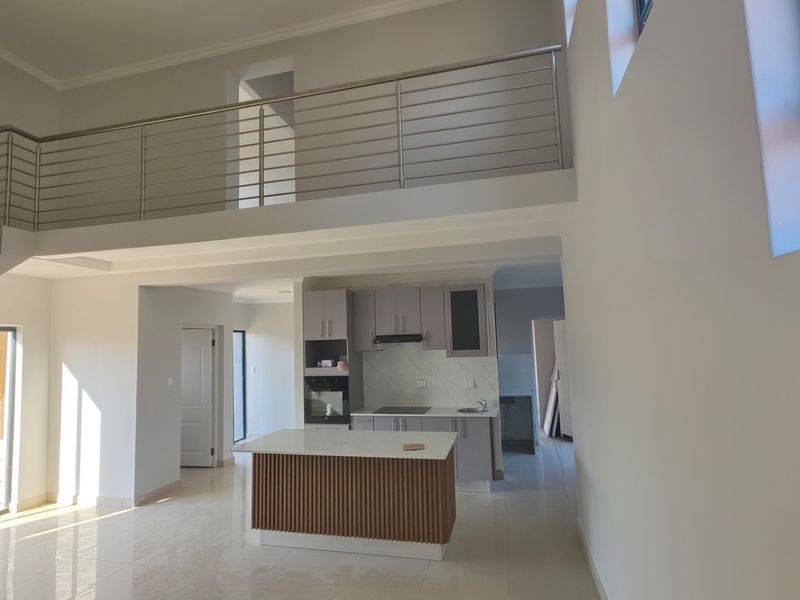 Spacious open-plan living area featuring a modern kitchen with a central island, built-in appliances, and a mezzanine level with a sleek metal balustrade.