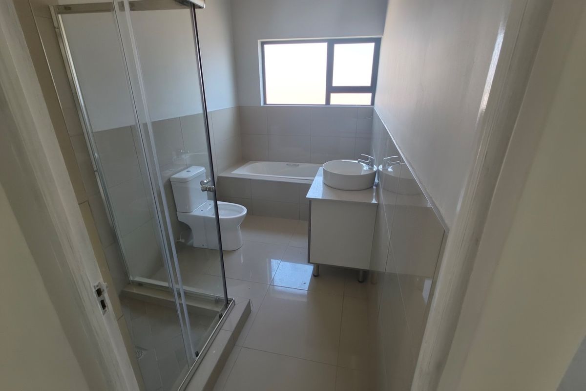 A clean, modern bathroom featuring a glass shower enclosure, a built-in bathtub, a vanity with a vessel sink, and neutral floor-to-ceiling tiling.