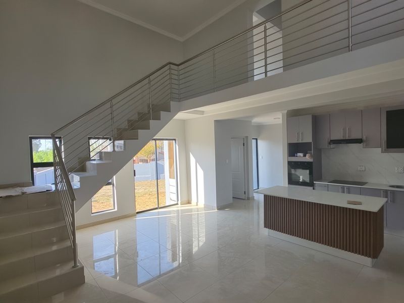 Spacious open-plan living area featuring a modern kitchen with island, sleek staircase with stainless steel railing, and large sliding doors leading to the garden.