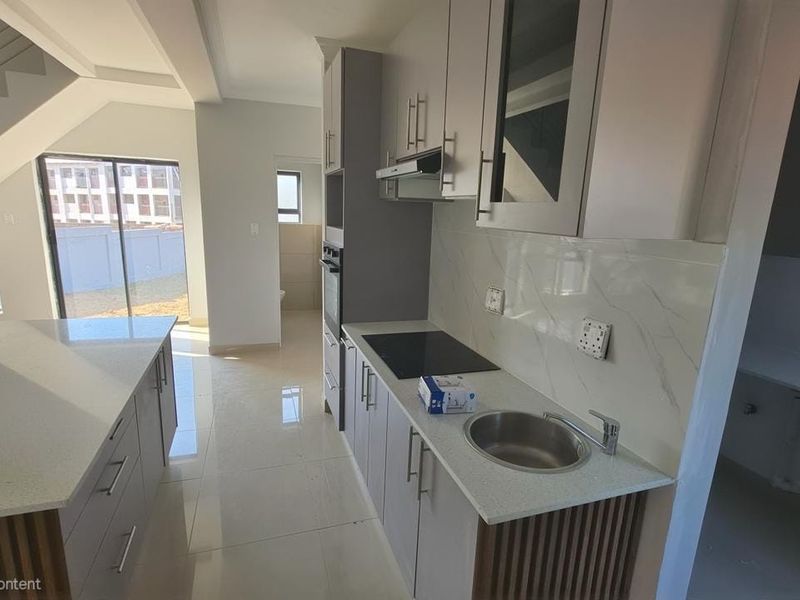 Modern kitchen featuring a central island, stone countertops, built-in cabinetry, integrated appliances, and a marble-look splashback, adjacent to an open-plan living area.