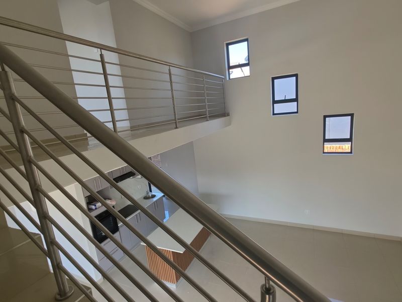 An open-plan living and kitchen area featuring a modern staircase with stainless steel balustrades, tiled floors, and a contemporary kitchen island.