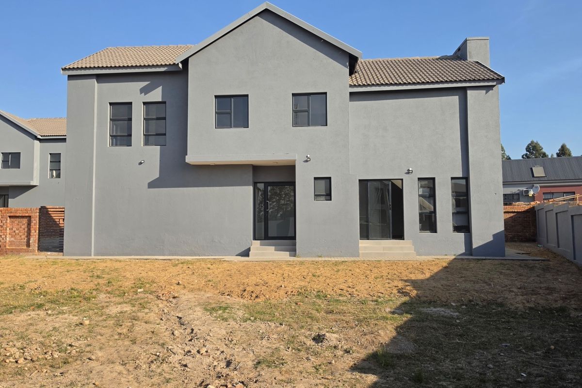 Rear view of a modern double-story house featuring a grey rendered facade, tiled roof, and access to an unlandscaped backyard area.