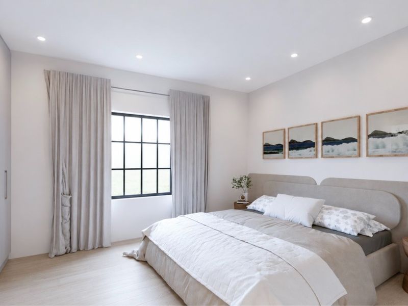 A modern, well-lit bedroom featuring neutral tones, built-in wardrobe storage, and a large grid-pattern window.