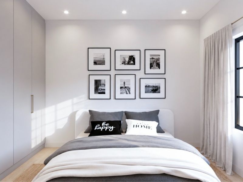 A modern, well-lit bedroom featuring built-in wardrobes, recessed downlighting, and a large black-framed window with neutral curtains.