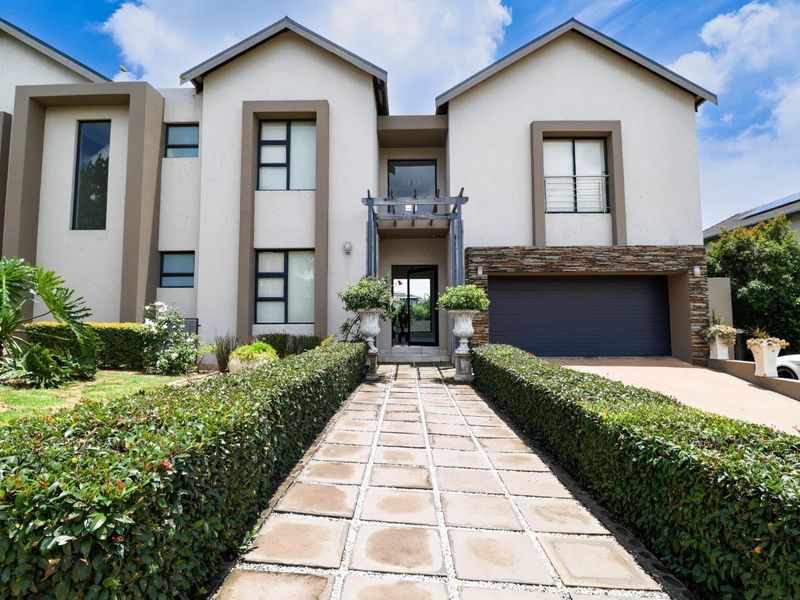 Modern double-story residential facade featuring a paved walkway, stone cladding accents, and an integrated double garage.