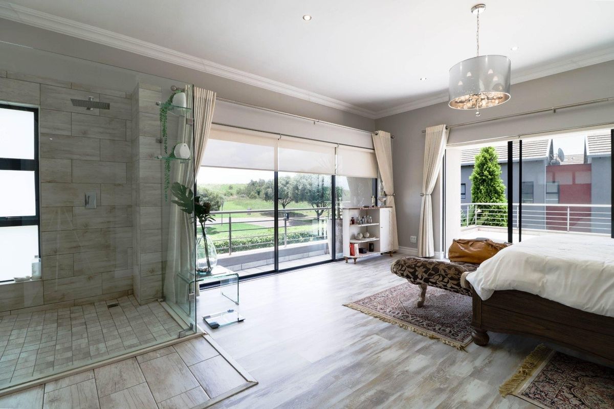 Spacious bedroom featuring an integrated walk-in shower, modern tiled flooring, and large sliding glass doors opening onto a private balcony with scenic views.
