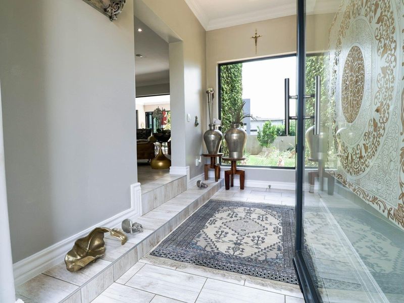 A bright and welcoming entrance hall featuring tiled flooring, a large glass pivot door, and a decorative feature wall.