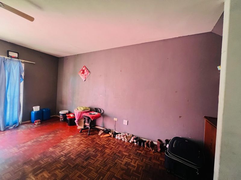 A living room area featuring traditional parquet flooring and a ceiling fan, currently requiring cosmetic updates to the wall finishes and flooring.