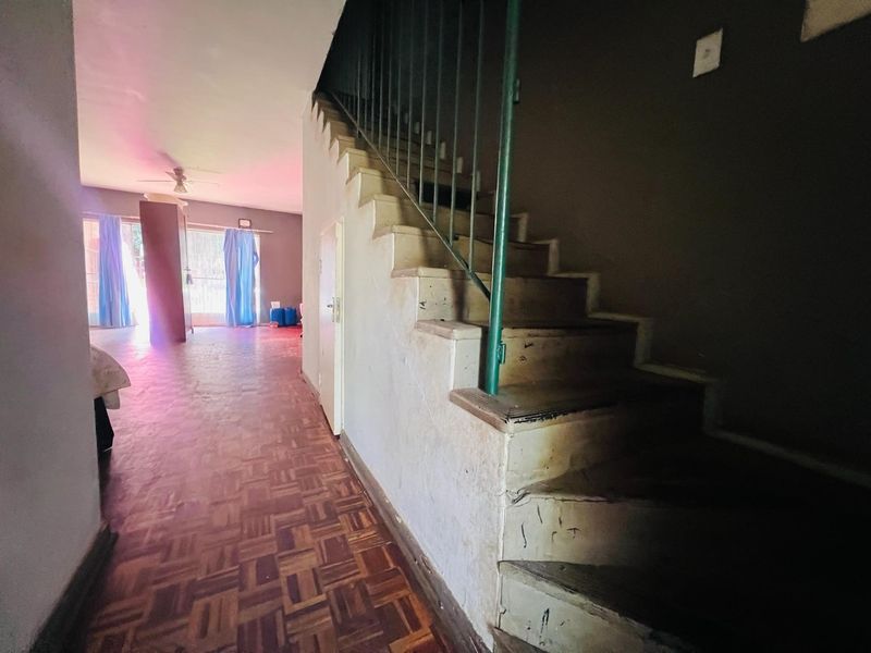 A hallway featuring a staircase with a metal balustrade and parquet flooring, leading into an open living area with a ceiling fan.