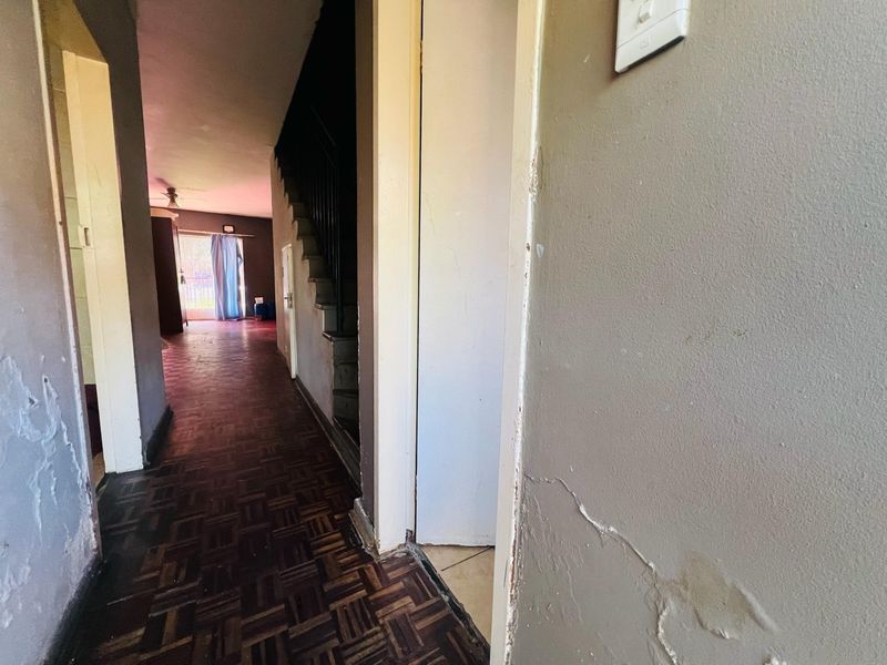 A hallway featuring parquet flooring and a staircase, showing significant signs of wear including peeling paint and damaged wall plaster.