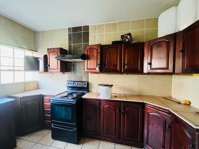 A dated kitchen featuring dark wood cabinetry, tiled countertops, and a freestanding electric stove with an extractor fan.